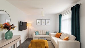 Un salon moderne avec un canapé blanc, un fauteuil jaune, une table basse et un téléviseur à écran plat fixé au mur.
