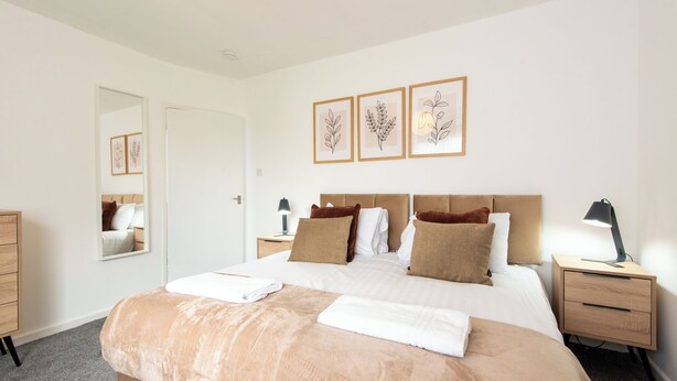 Une chambre à coucher bien rangée, avec un grand lit, des tables de chevet, une commode et des œuvres d’art encadrées accrochées au mur.
