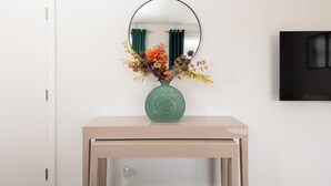 Une pièce avec une console de couleur beige, un vase vert orné de fleurs et un miroir rond accroché au mur.