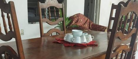 A dining table with six wooden chairs, a set of white cups and saucers, and a red napkin.