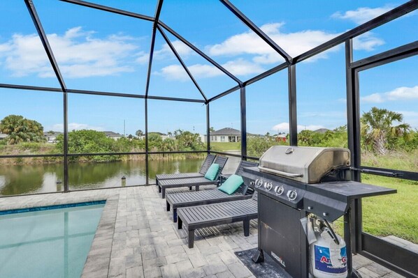 A covered outdoor area with a grill, lounge chairs, and a view of a body of water.