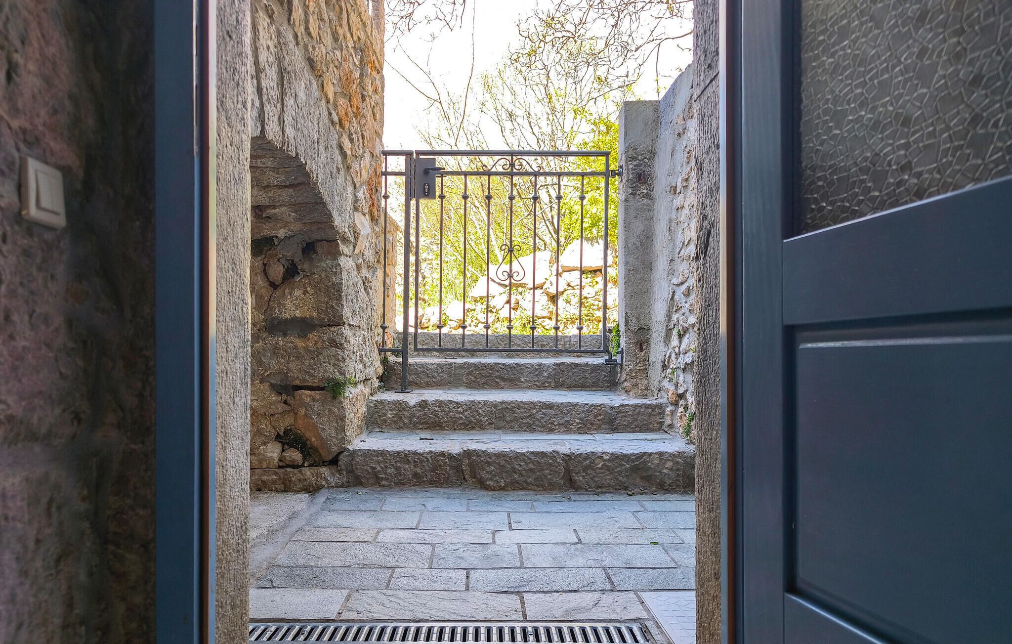 Eine steinerne Treppe führt zu einem verschlossenen Eingang, wobei ein Metallgitter und ein Türrahmen sichtbar sind.