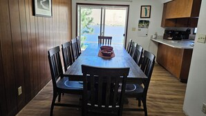 Een eethoek met een houten tafel en stoelen, uitzicht op een waterpartij door een glazen deur, en een keuken met houten kastjes en apparatuur.