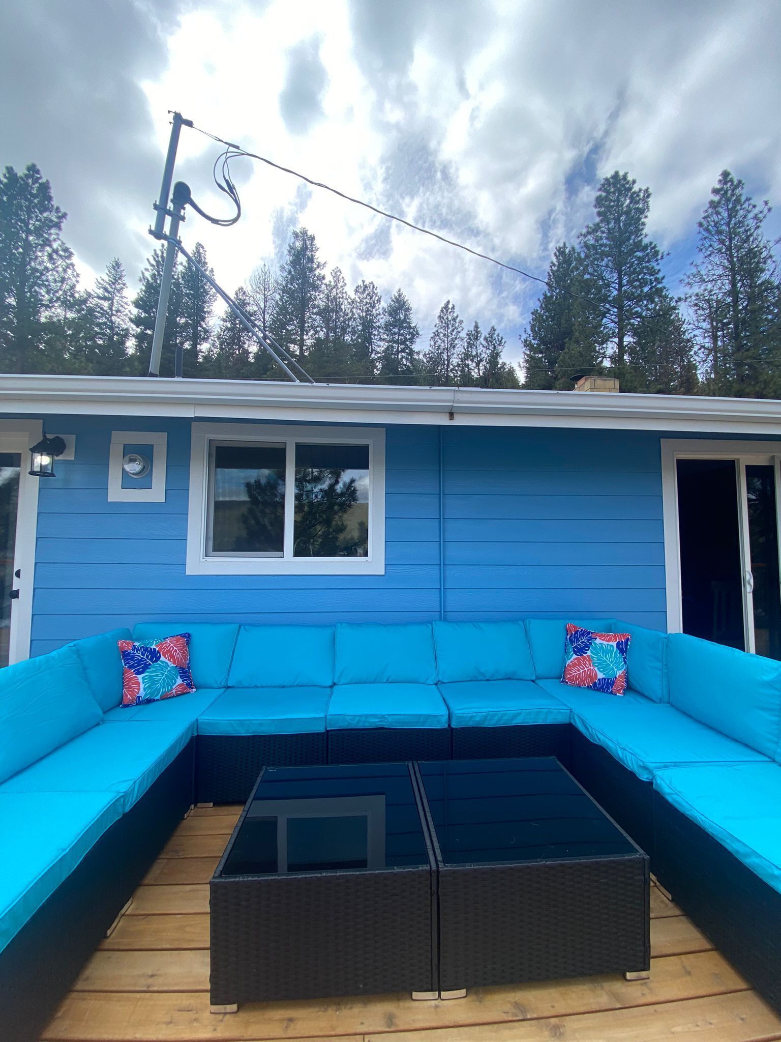 A blue exterior with a large window, a black wicker table, and a blue sofa with colorful pillows.