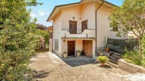 Un edificio a due piani con un cortile in pietra, persiane in legno alle finestre e piante in vaso all'ingresso.