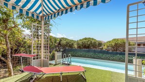 Area piscina con una sedia a sdraio rossa, un tenda a righe blu e bianche e vista su un giardino fiorito.