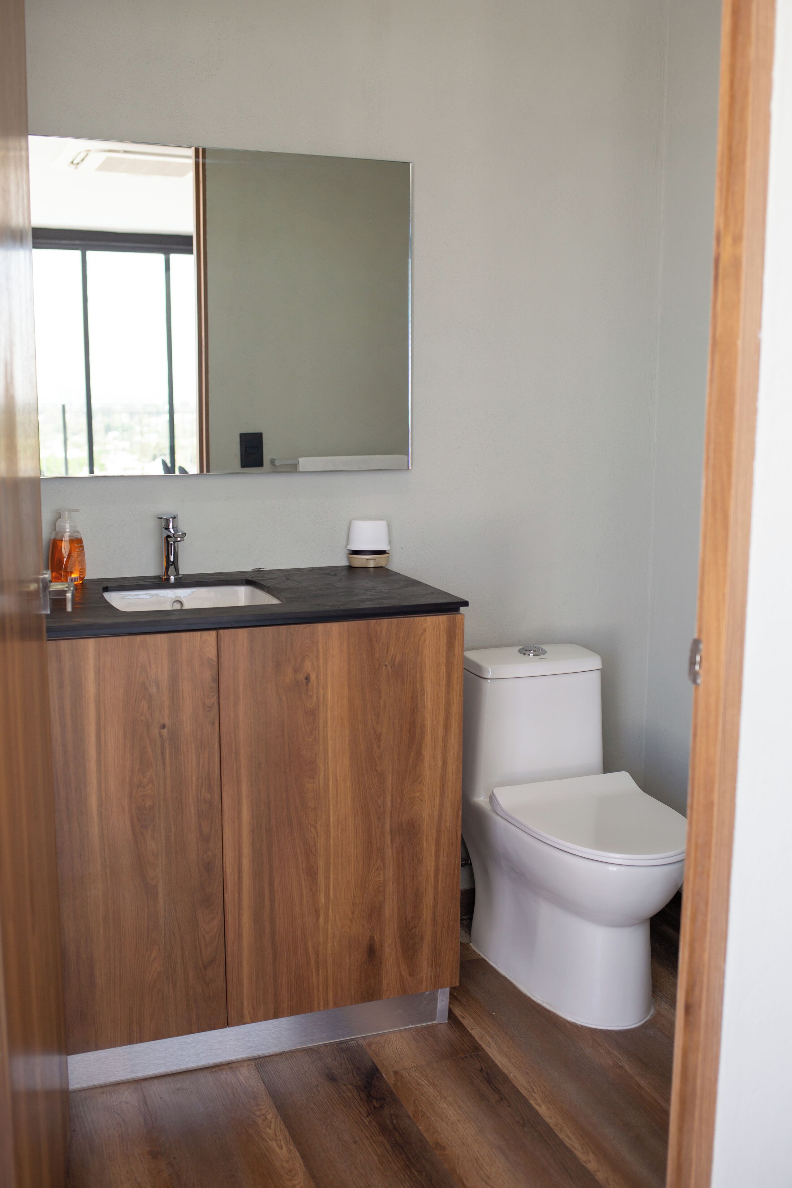 Un baño moderno con tocador de madera, lavamanos, espejo y retrete.
