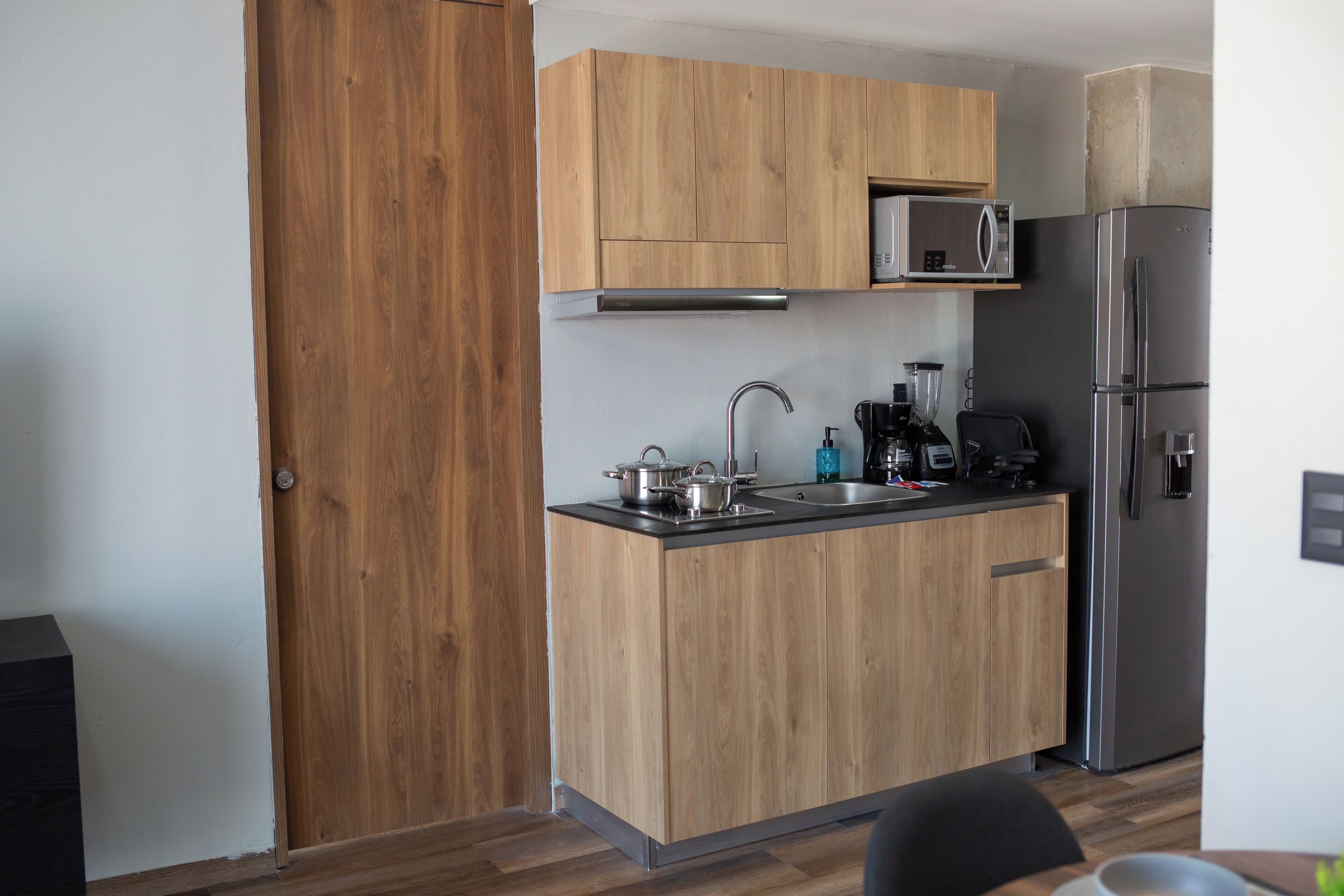 A compact kitchen with wooden cabinets, a stainless steel refrigerator, a microwave, and a coffee maker.