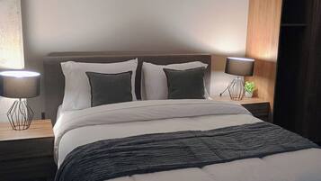 Een moderne hotelkamer met een groot bed, twee nachtkastjes met lampen, een houten garderobe, en een opgemaakt bed met opgerolde handdoeken.