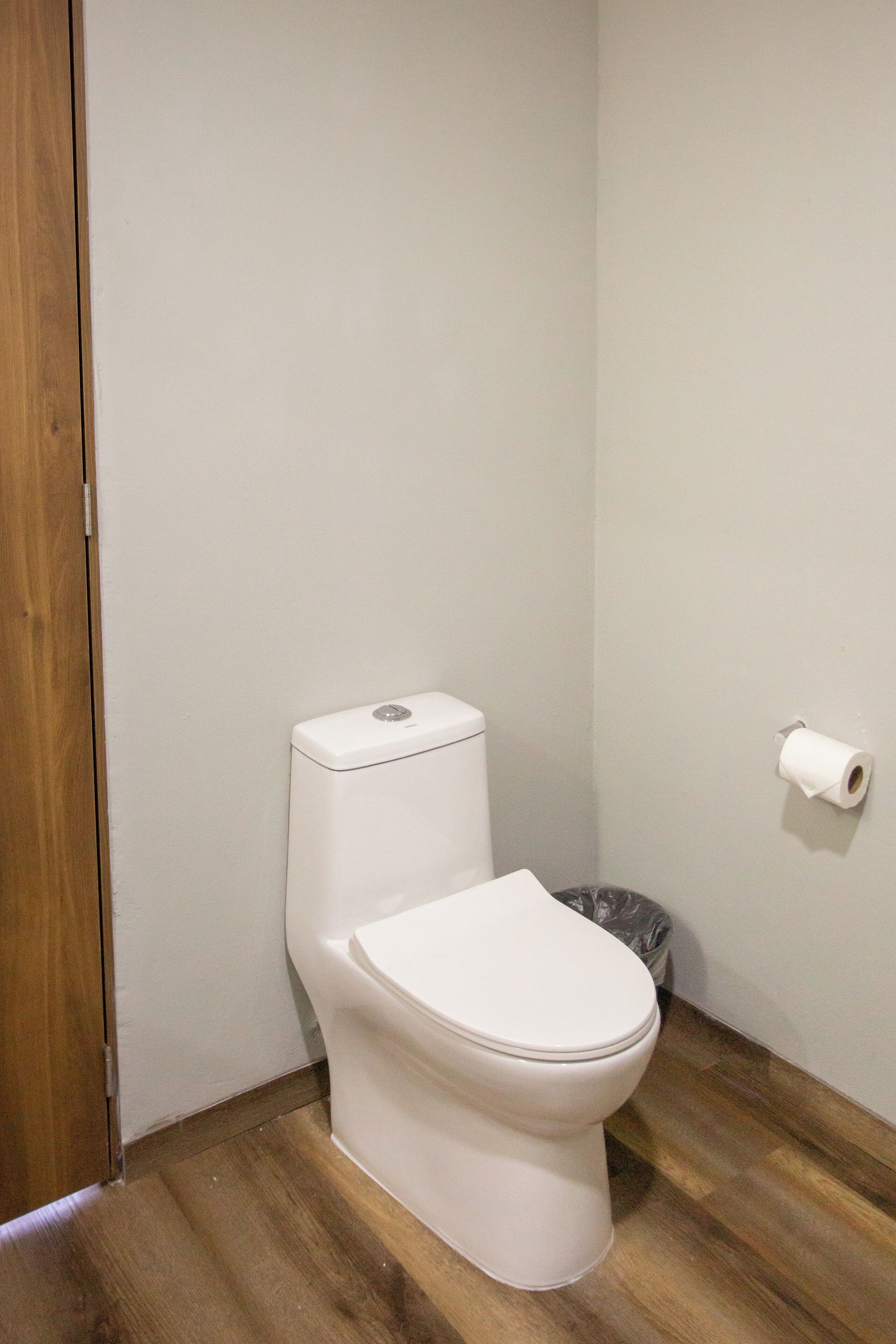 A small, clean bathroom with a white toilet, a wooden floor, and a paper towel dispenser on the wall.