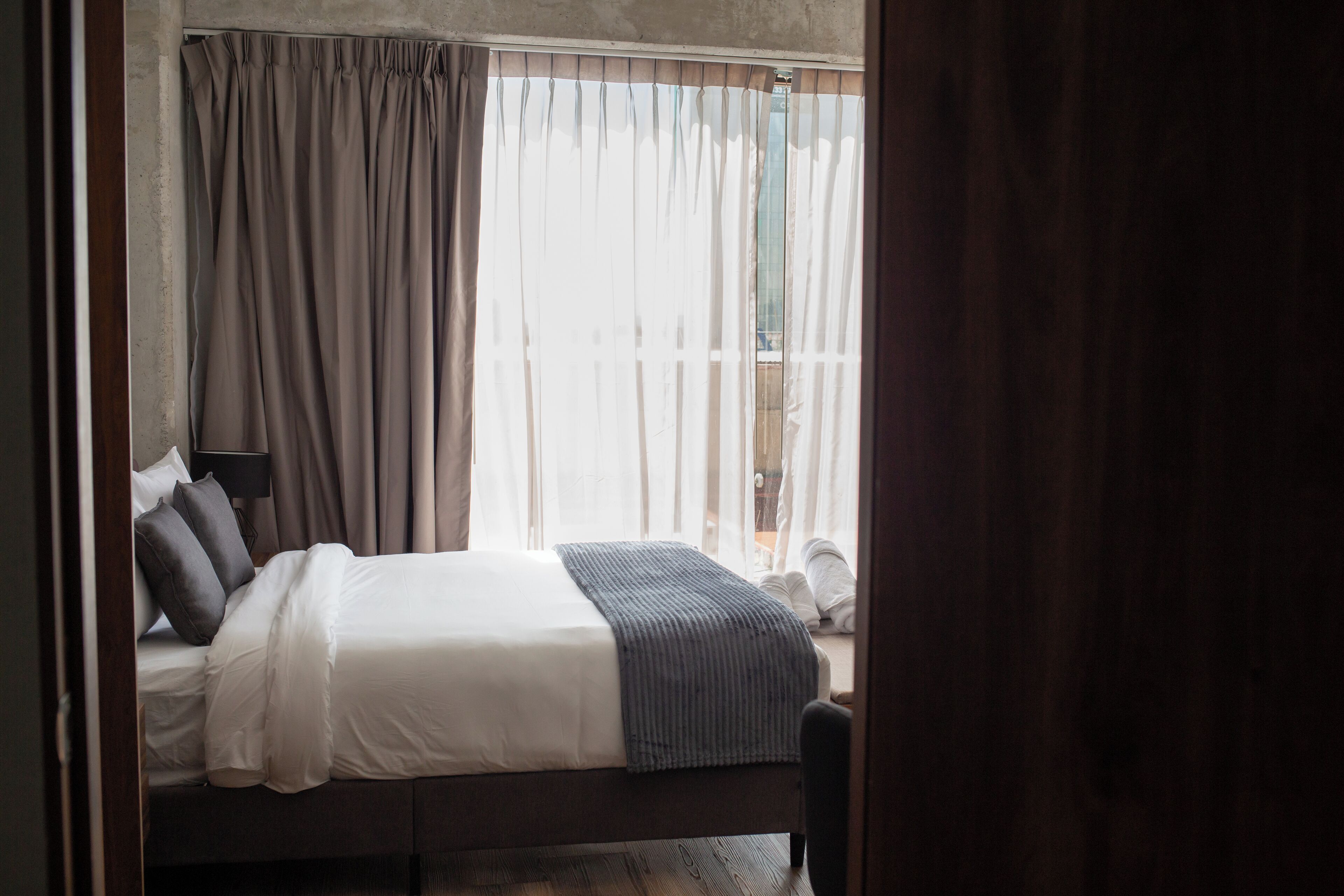 Un dormitorio con cama, cortinas, lámpara y vistas al exterior.