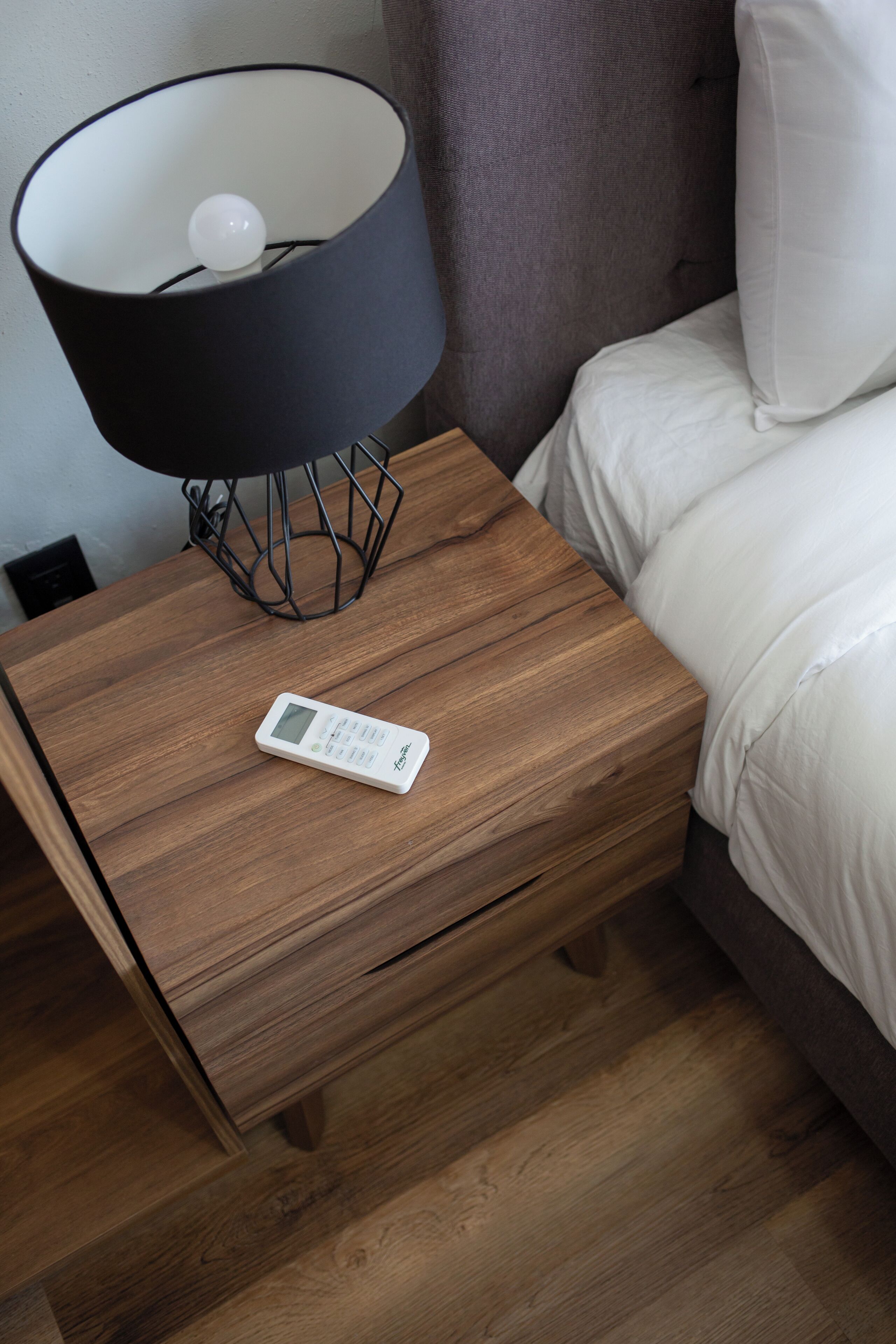 Une table de chevet en bois, avec une lampe noire et un thermostat numérique.