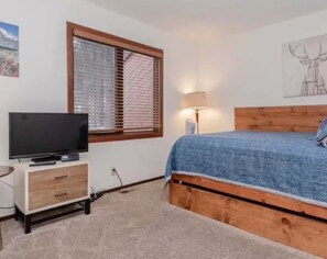 A bedroom with a bed, a TV on a wooden cabinet, a window with blinds, and a lamp. - Cozy, Clean & Conveniently Located Townhome near Eagle Lodge (Mammoth Lakes)