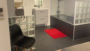 Une salle de bain moderne avec une douche, un lavabo et un miroir. Il y a un tapis rouge sur le sol et une chaise noire.