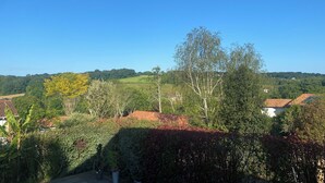 Un paysage rural caractérisé par un ciel bleu dégagé, une variété d’arbres et une maison avec un toit rouge.