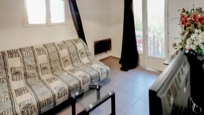 Una sala de estar con un sofá estampado, un televisor de pantalla plana y un ventanal con cortinas.
