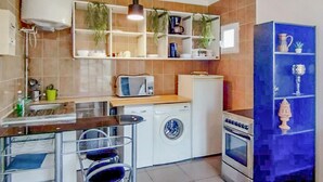 Cocina compacta con lavadora, microondas y estufa. Hay repisas con plantas y utensilios de cocina.