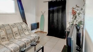 Un salón con un sofá estampado, una mesita, un televisor de pantalla plana, un radiador y una cortina.