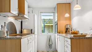 Een kleine keuken met witte kastjes, een raam, een koffieapparaat en een brood op het aanrecht.
