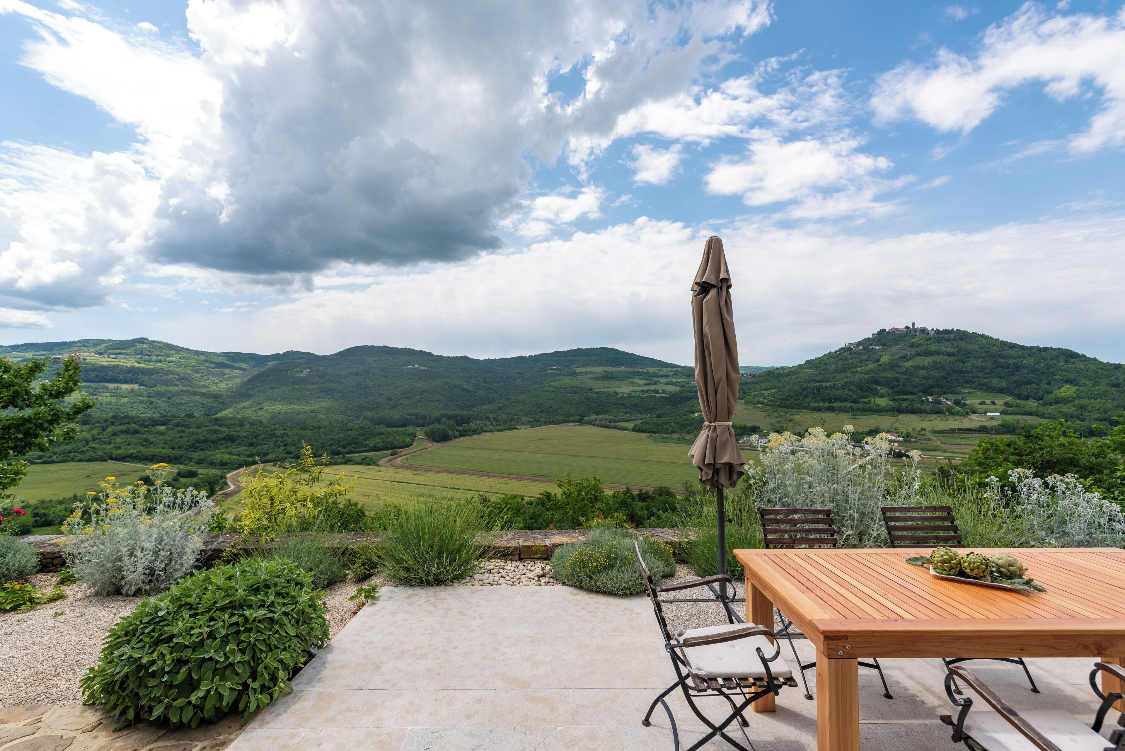 A patio with a table and chairs, overlooking a scenic landscape with hills and fields.