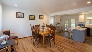 Un comedor con mesa y sillas de madera, una cocina con una isla central, y vistas al exterior.