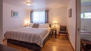 Un dormitorio con cama, mesitas de noche, una silla y una ventana con cortinas.