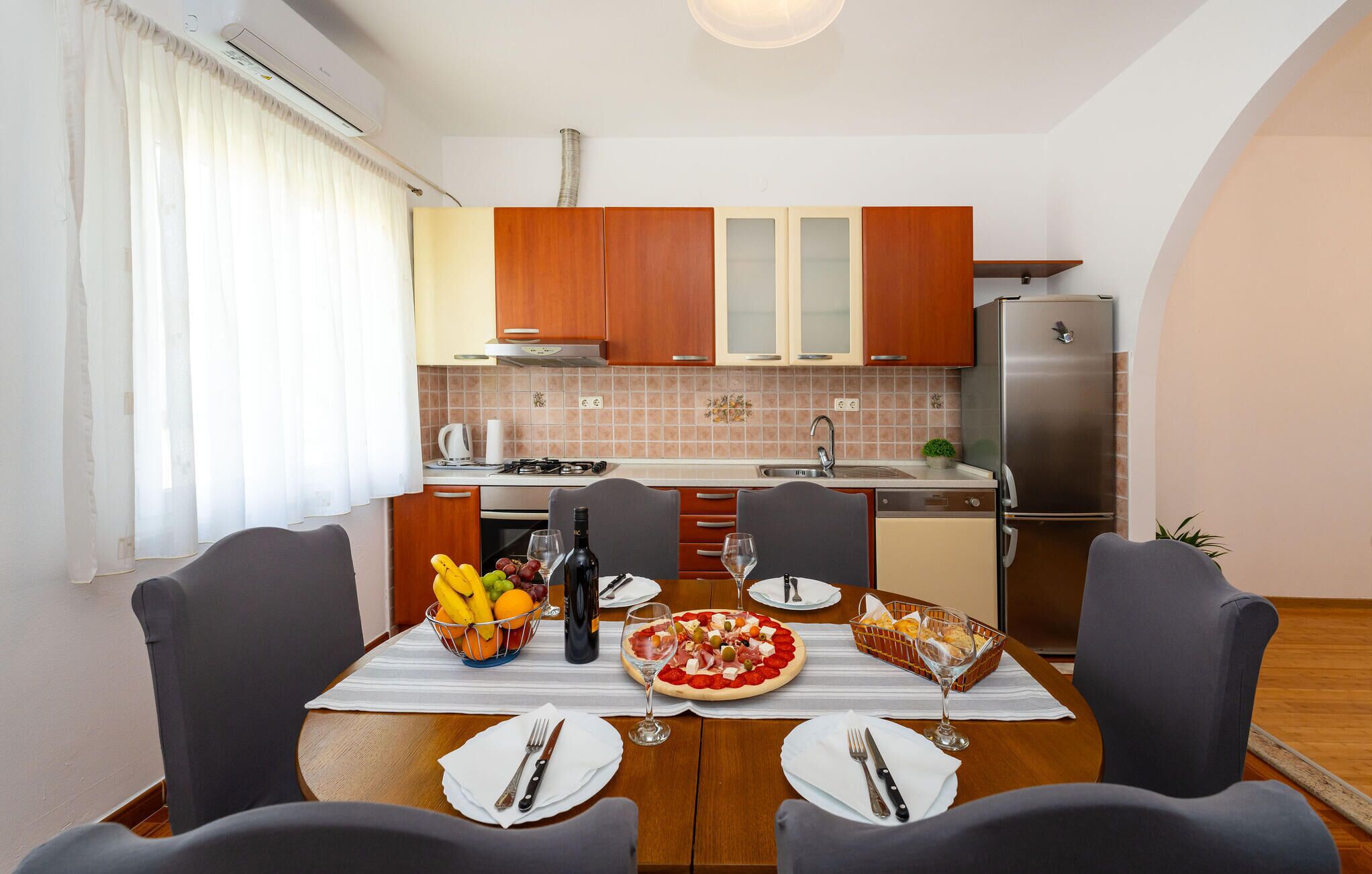 Een compacte keuken met houten kastjes, een roestvrijstalen koelkast en een eettafel gedekt voor twee personen, compleet met borden, bestek en een pizza.