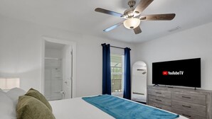 Un dormitorio con cama, ventilador de techo, televisión y cómoda.