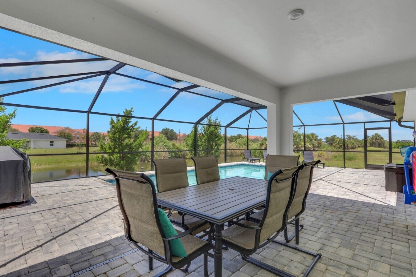 A covered patio with a pool table, chairs, and a grill.