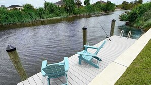 Un muelle de madera con dos sillas Adirondack y una caña de pescar.