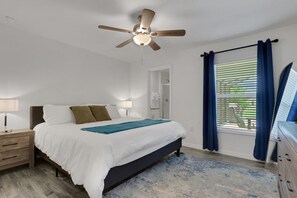 A bedroom with a bed, nightstands, a ceiling fan, a window with curtains, and a dresser. - New Spacious Home w/ Heated Saltwater Pool & Private Pier! (Cape Coral)