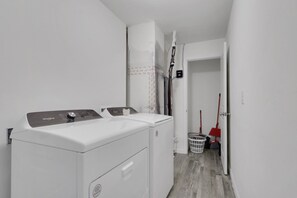 A laundry area with a front-loading washer and dryer, a mop, and a broom.