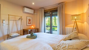 A hotel room with a bed, a desk with a lamp, an air conditioning unit, a window with curtains, and a view of greenery outside. - 5 bedroom amazing home in Restabal (Restabal)