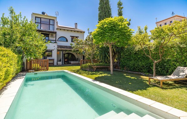 Relax in a serene backyard with a swimming pool, lush greenery, and a clean deck.