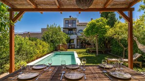 A wooden pergola with a pool table set for dining, surrounded by lush greenery and a view of a white building with a balcony. - 5 bedroom amazing home in Restabal (Restabal)