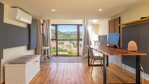 A modern room with a wooden floor, a desk with a computer, a cushioned bench, and a large window offering a view of the countryside. - 5 bedroom amazing home in Restabal (Restabal)
