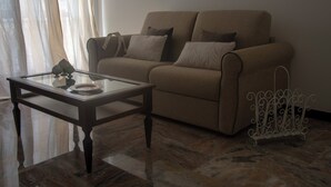 En stue med en beige sofa, et glasbord og et hvidt metalstativ.