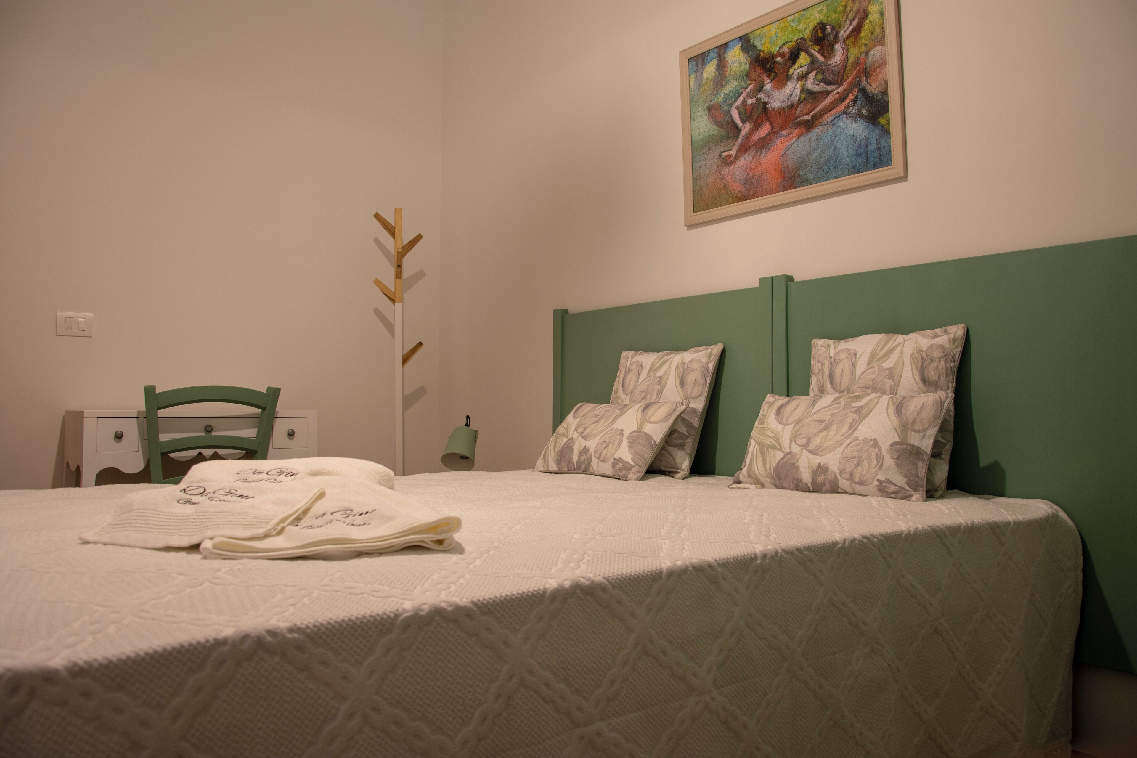 Un letto rifatto con cuscini a motivi floreali, una testiera verde e un quadro appeso sopra.