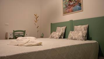 Un letto rifatto con cuscini a motivi floreali, una testiera verde e un quadro appeso sopra.