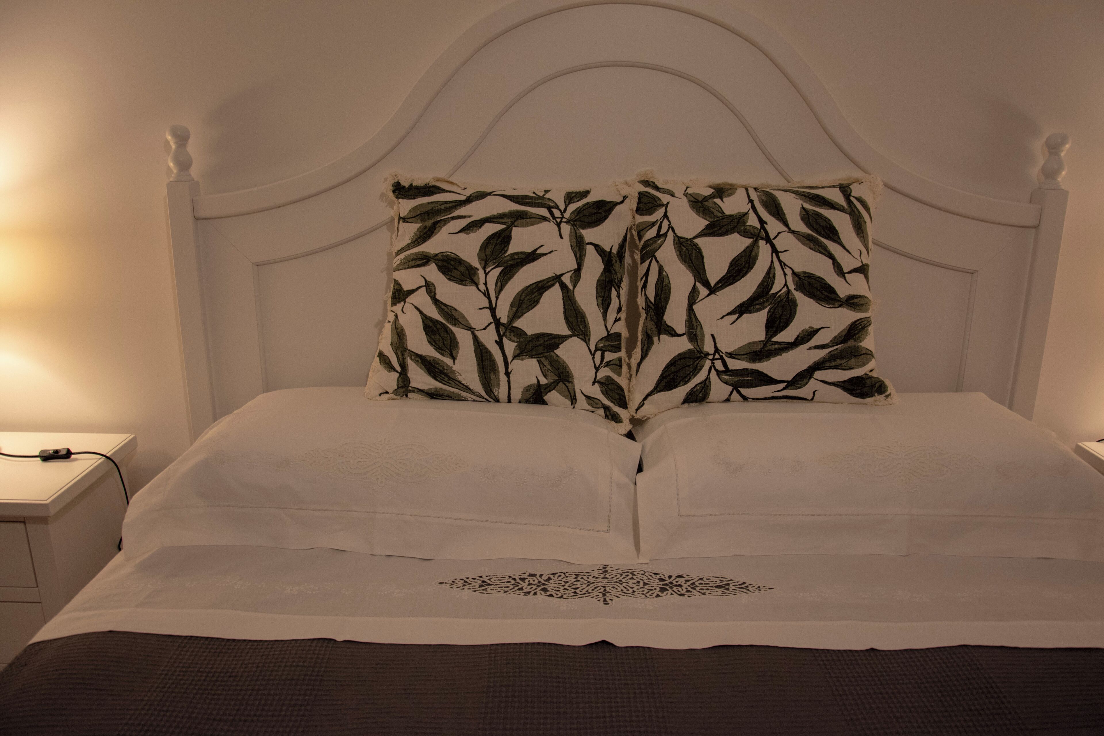 A bed with a white headboard, two pillows with a leaf pattern, and a decorative bed runner.