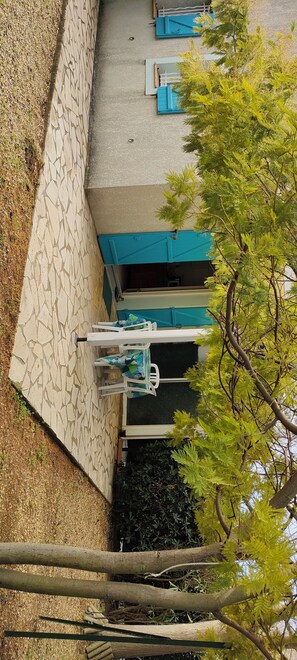 A patio area with a stone floor, a table with chairs, and a building with blue doors. - Maison Bord de mer Vendres Plage (Vendres)