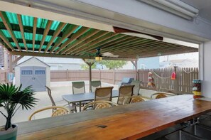 Un patio al aire libre con una mesa y sillas de madera, un área de estar cubierta y vista a un jardín trasero.