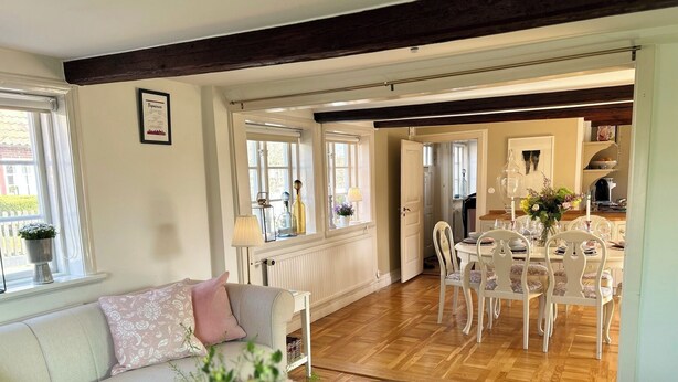 A cozy living room with a sofa, a coffee table with a vase of flowers, and a dining area with a table set for four. - Beautiful 1700 century house in the heart of Viken. Pets Allowed! (Skåne län)