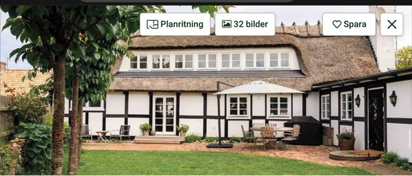 Una casa tradizionale a mezzo legno con struttura in bianco e nero, un tetto di paglia, un patio con mobili da esterno e un giardino.