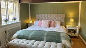 A bedroom with a tufted headboard, a bedside table with a lamp, a window with flowers, and a radiator. - Beautiful 1700 century house in the heart of Viken. Pets Allowed! (Skåne län)