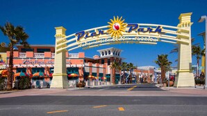 The entrance to Pier 70, Panama City Beach, Florida, with a prominent sign and palm trees. - PRICE REDUCTION!  Polynesian Village pool side! Walking distance to Pier Park (Panama City Beach)