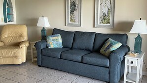 A living room with a grey sofa, two matching armchairs, and a small white side table with a lamp. There are two framed wall art pieces above the sofa. - PRICE REDUCTION!  Polynesian Village pool side! Walking distance to Pier Park (Panama City Beach)