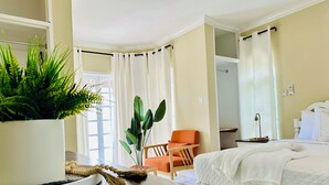 Een hotelkamer met een bed, een stoel, een tafel met een plant en een raam met gordijnen.