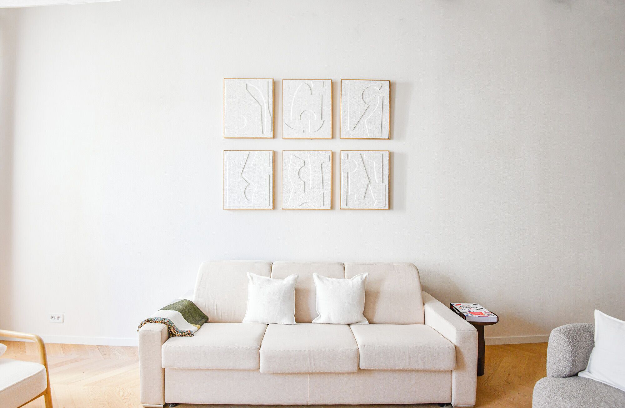 Un salon minimaliste avec un canapé blanc, une petite table d’appoint et un fauteuil gris.