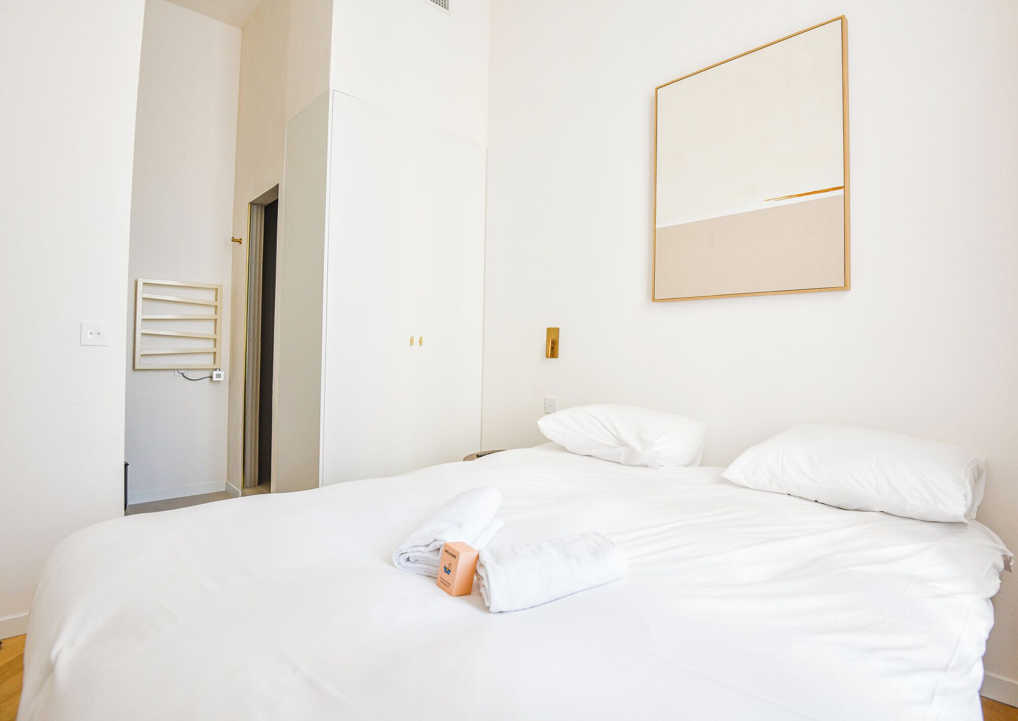 A hotel room with a bed, a bedside table, a wall-mounted mirror, and a door leading to another room.